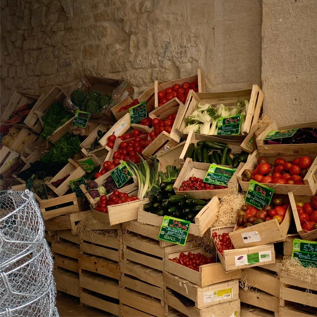 A pile of wooden crates filled with various fruits and vegetables is stacked haphazardly in a small market stall.