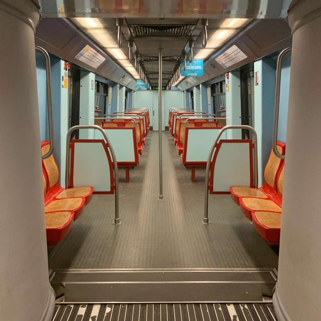 An empty train carriage, brightly coloured with red and orange seats and pale blue walls.